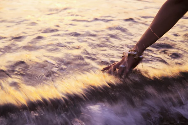 Frau berührt Meereswelle bei Sonnenuntergang. verschwommener Hintergrund — Stockfoto
