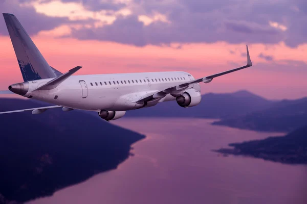 Flugzeug fliegt bei violettem Sonnenuntergang über Berge und Meer — Stockfoto