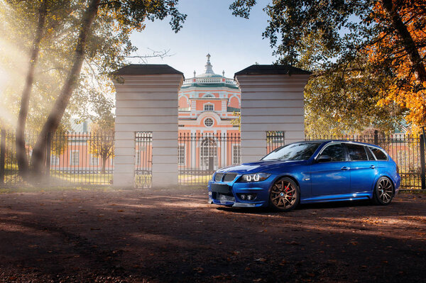 Синий автомобиль BMW 3 серии E91, стоящий рядом с осенним лесом парка
