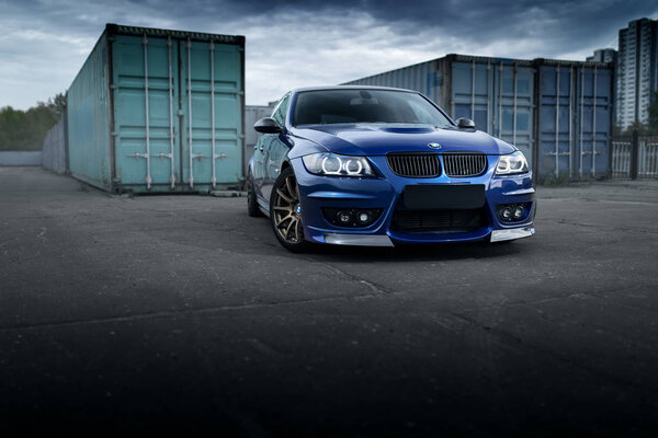 Синий автомобиль BMW 3 серии E91, стоящий рядом с контейнерами

