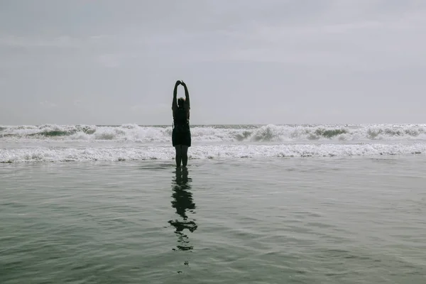 La donna è in piedi sulla spiaggia di mare. Braccia tese sollevate . — Foto Stock