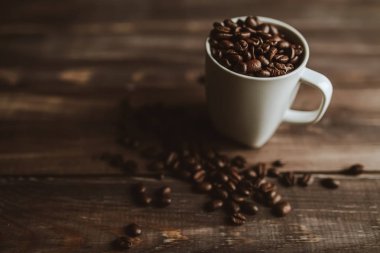 Kavrulmuş kahve çekirdekleri ahşap arka plan, beyaz Kupası