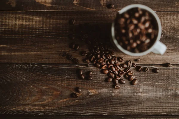 Granos de café tostados en taza blanca en fondo de madera — Foto de Stock