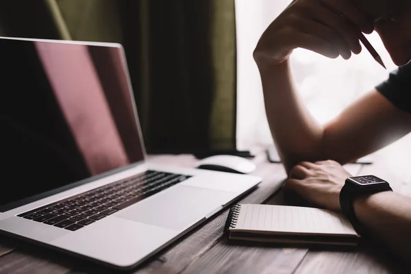 O homem está escrevendo no bloco de notas do esboço e usando o computador portátil e no escritório home. Local de trabalho estilo de vida freelance — Fotografia de Stock