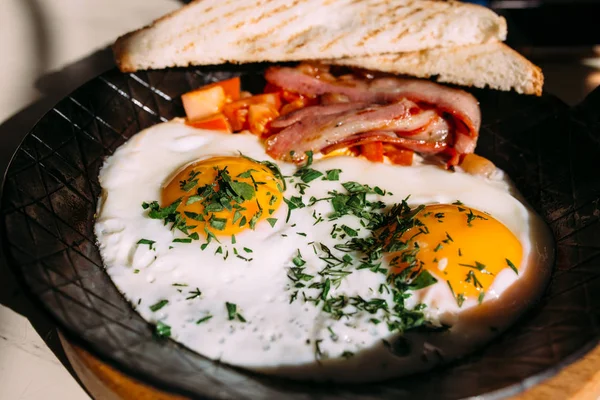 Smažená vejce, slanina, rajčata na přípitek. Klasická snídaně jídlo v litinové pánvi — Stock fotografie