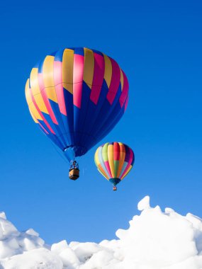 İki renkli sıcak hava balonu kışın karlı arazide uçuyor.