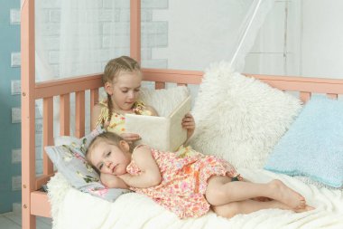 Ablası küçük kız kardeşine kitap okuyor.