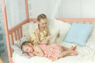 Ablası küçük kız kardeşine kitap okuyor.