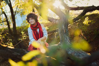 Bir ağacın altında oturup sonbahar ormandaki kıvırcık kız.