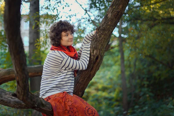 秋の森の木に座っている巻き毛の少女 — ストック写真