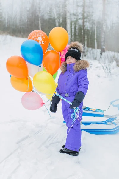Menina alegre caminha no inverno na floresta na montanha. ela segura na mão um monte de balões multicoloridos . — Fotografia de Stock