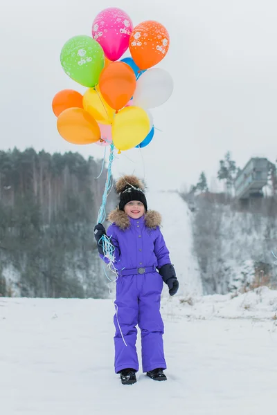 Menina alegre caminha no inverno na floresta na montanha. ela segura na mão um monte de balões multicoloridos . — Fotografia de Stock