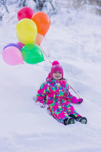 Dziewczynka w kolorowy komplet leżącego w śniegu, w lesie zimą z kolorowych kulek — Zdjęcie stockowe