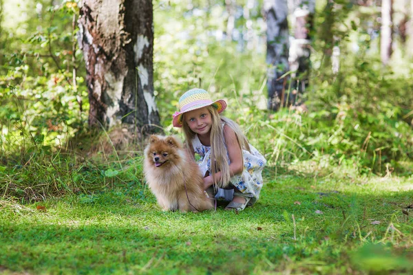 Meisje loopt met haar geliefde hond in het bos in een zonnige zomerdag. Meisje in haar Spitz knuffelen hoed. — Stockfoto