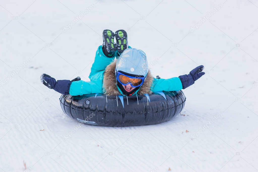 cheerful girl in a helmet and glasses riding on a sled with high mountains