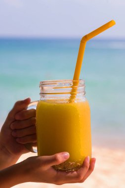 arka plan tropikal turkuaz denizin üzerinde elinde bir turuncu vitamini mango suyu bir cam tüp