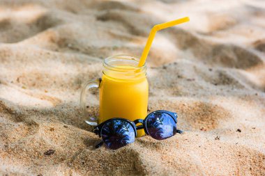 vitamini mango suyu tropikal turkuaz denizin kıyısında kum üzerinde bir saman turuncu gözlüklü bir cam.