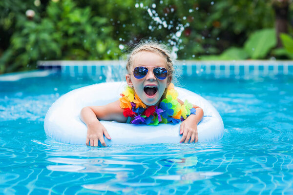 little girl in sunglasses floating on the circle in the pool at a resort in the tropics