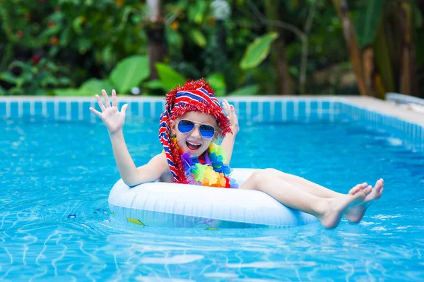 Dziewczynka w okulary przeciwsłoneczne i czerwoną czapkę unoszące się na kole w basenie w ośrodku w tropikach — Zdjęcie stockowe