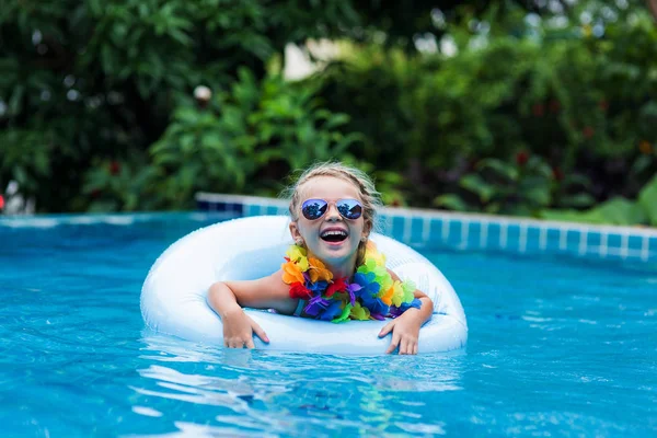 Dziewczynka w okulary unoszące się na kole w basenie w ośrodku w tropikach — Zdjęcie stockowe