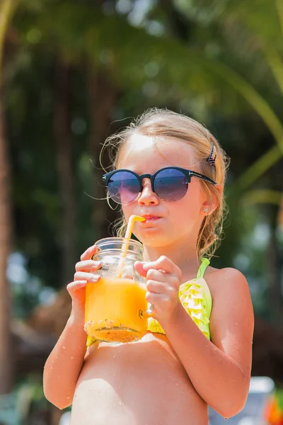 Chica en gafas de sol y bañador bebiendo un vaso de jugo de mango junto al mar, en la playa — Foto de Stock