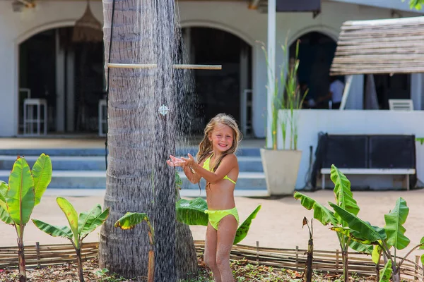 Niña se para en la ducha en un traje de baño en la playa en un resort — Foto de Stock
