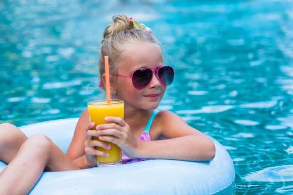 Mała dziewczynka leżąc na nadmuchiwany pierścień w basenie. W rękach kieliszek soku z mango. Wakacje. — Zdjęcie stockowe