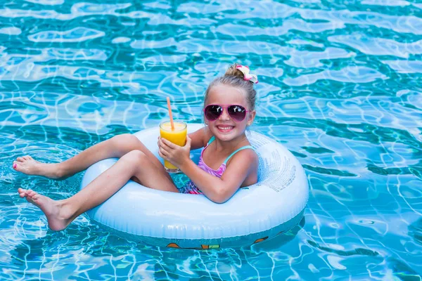 Mała dziewczynka leżąc na nadmuchiwany pierścień w basenie. W rękach kieliszek soku z mango. Wakacje. — Zdjęcie stockowe
