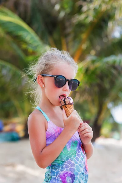 Gadis kecil yang lucu berkacamata hitam dengan es krim di pantai dengan pohon palem di laut. surga . — Stok Foto