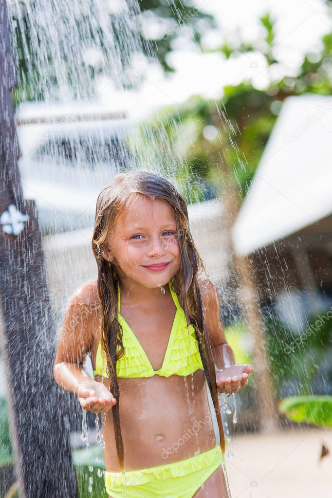 Pretty smiling girl standing under the spray of water in the shower on the beach