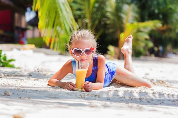 Pequeña linda chica en la arena en la playa en gafas de sol con un vaso de jugo de cóctel exótico — Foto de Stock