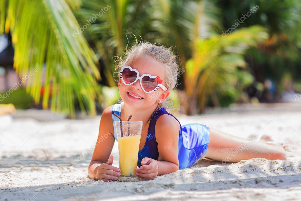 little cute girl on the sand at the beach in sun glasses with a glass of exotic cocktail juic