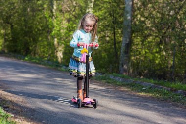 Küçük çocuk bir scooter bir şehir parkı güneşli yaz gününde binmek için öğrenme. Çocuklar açık havada oynar. Etkin boş ve çocuklar için açık spor.