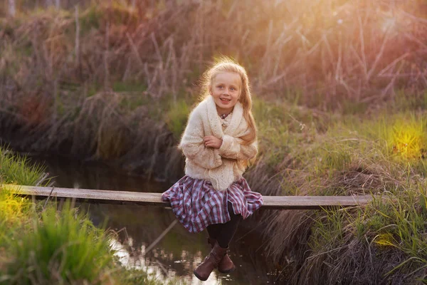 森で夕方には夕日で橋上に座ってロシアのスカーフでかわいい陽気な女の子 — ストック写真