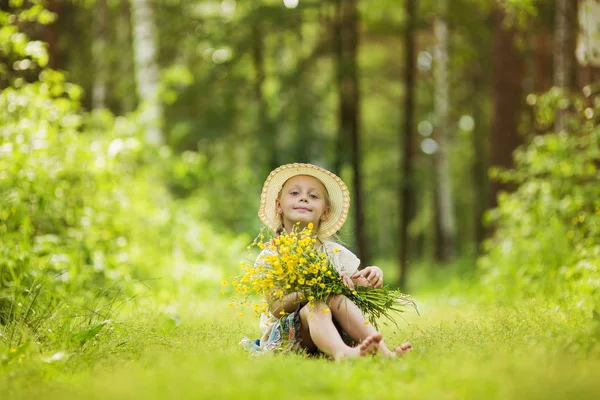 Uma menina sorrindo pequena bonito no campo de girassóis segurando um monte enorme de flores em um horário de verão ensolarado . — Fotografia de Stock