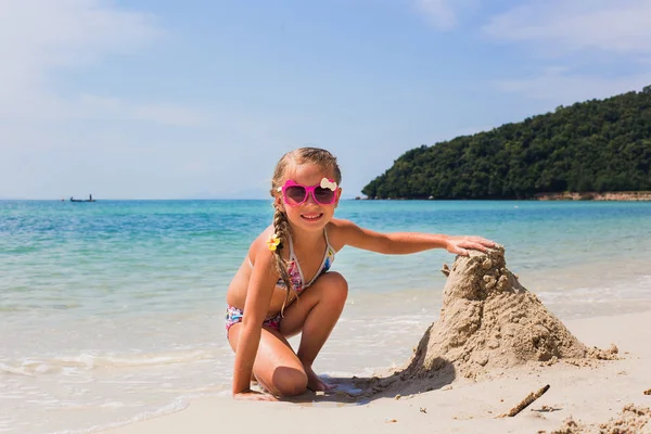 Милая маленькая девочка играет с песком на тропическом пляже — стоковое фото