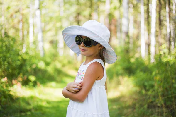 Retrato de uma menina bonita usando óculos de sol e um chapéu em uma floresta ensolarada de verão — Fotografia de Stock