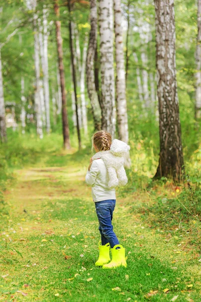 Chica con un juguete favorito en el bosque en un día de verano. vista posterior . Imágenes de stock libres de derechos