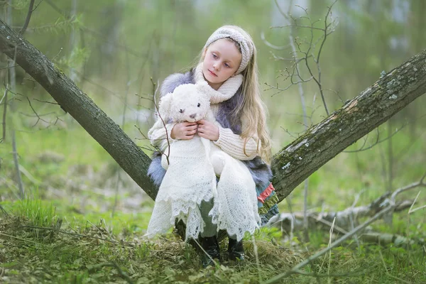 Linda niñita sosteniendo un oso de peluche. Se sienta en un árbol en el bosque, se entristece y llora . —  Fotos de Stock