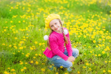 İki kuyruklu ile sarı şapkalı şirin güzel kız sarı dandelions alanında oturur
