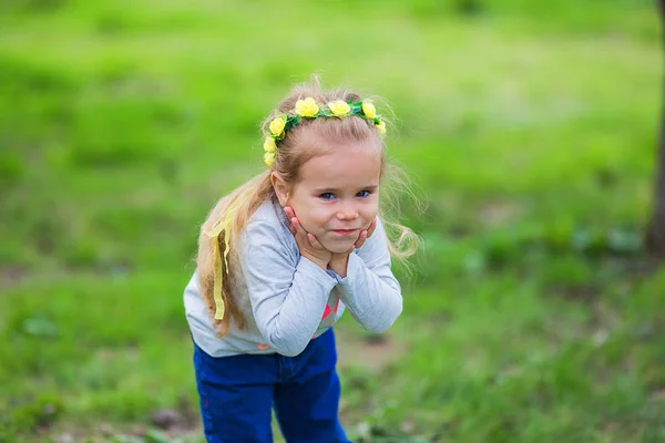 Portret van een schattig klein meisje in een krans van bloemen in een zomer-park — Stockfoto