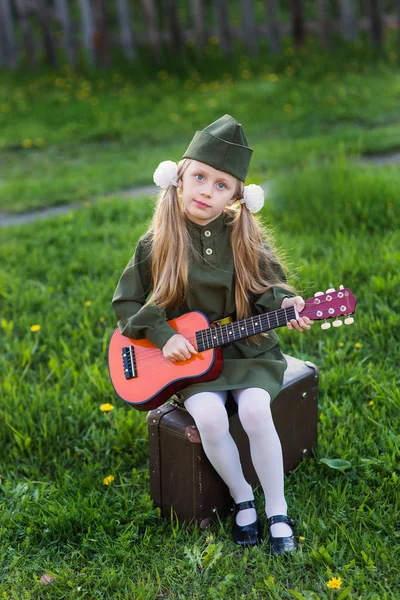 Nettes kleines Mädchen in Uniform für die Feiertage des Sieges mit Gitarre. Russland. — Stockfoto