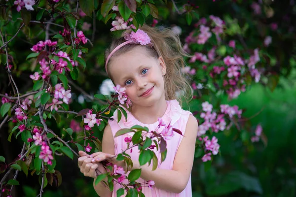 Mooie glimlachend schattig meisje met lang krullend haar tijdens de bloei roze appels — Stockfoto
