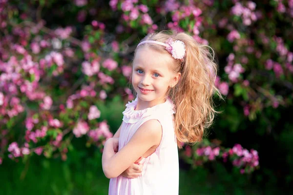 Όμορφη χαμογελώντας χαριτωμένο κορίτσι με μακριά σγουρά μαλλιά στην ανθοφορία ροζ μήλα — Φωτογραφία Αρχείου