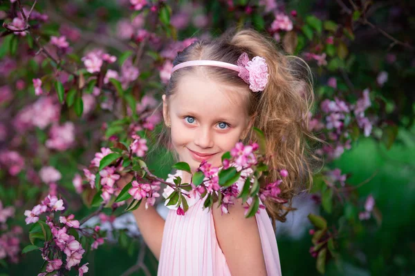 Krásný úsměv roztomilá dívka s dlouhými kudrnatými vlasy v kvetoucí růžové jablka — Stock fotografie