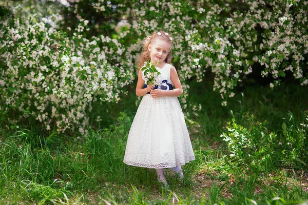 Krásná roztomilá dívka v krásné krásné bílé šaty s kyticí v kvetoucí jabloňový sad za slunečného dne — Stock fotografie