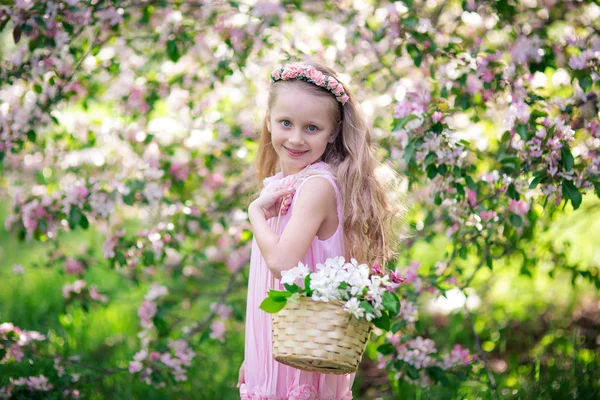 Schöne lächelnde süße Mädchen mit einem Korb voller Blumen in einem blühenden Apfelbaum an einem Sommertag — Stockfoto