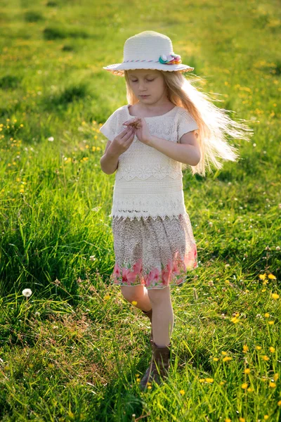 Menina bonita bonita em um chapéu com cabelos longos andando através de um campo em um estilo rústico em um dia ensolarado de verão — Fotografia de Stock