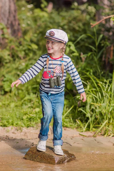 Ein kleines fröhliches Mädchen in Matrosenuniform und Seemütze steht am Ufer — Stockfoto