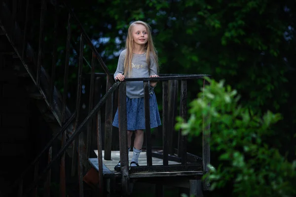 Ein nettes kleines Mädchen steht an einem Sommerabend auf einer antiken Treppe in einem Dorf — Stockfoto
